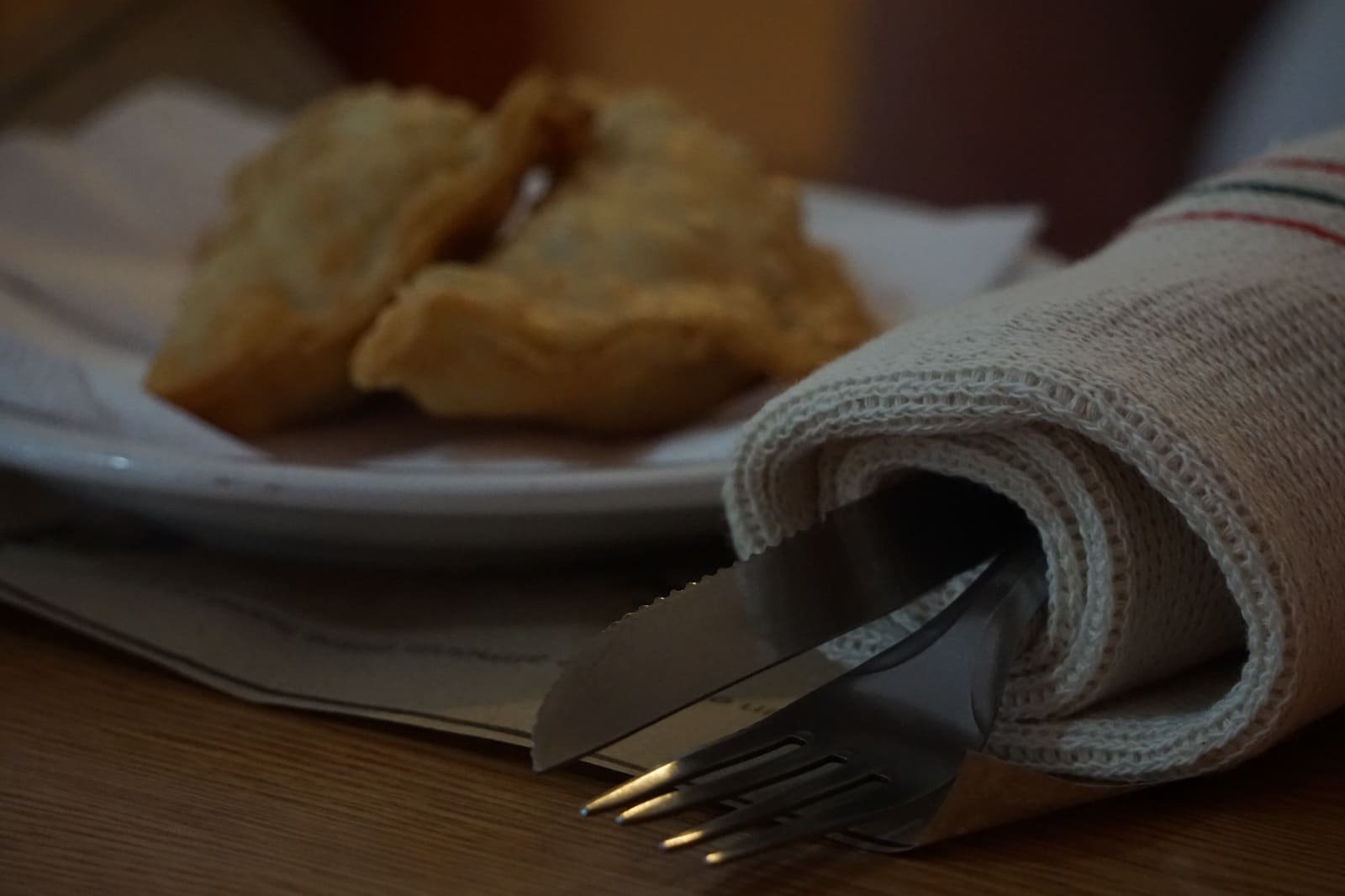 Ambiente de peña argentina auténtica con empanadas doradas y cubiertos elegantemente presentados envueltos por las rejillas Franciotex, que aportan un toque de limpieza y tradición a la mesa